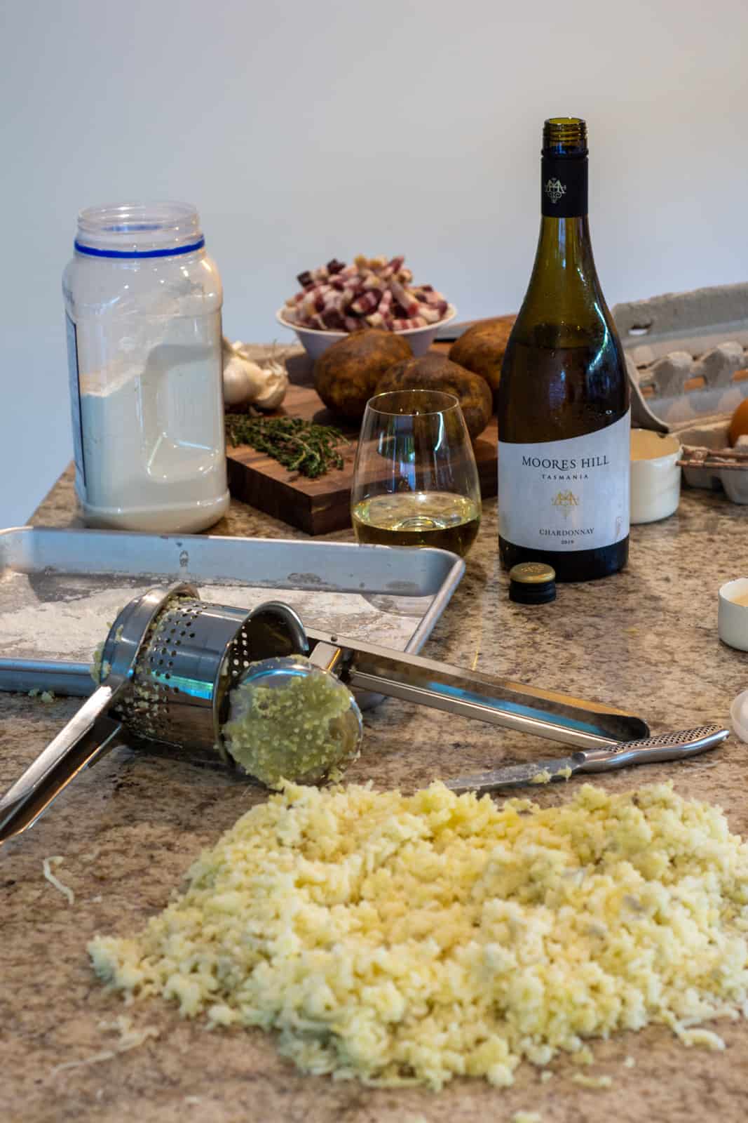 potato being riced for gnocchi on kitchen worktop with multiple ingredients in background