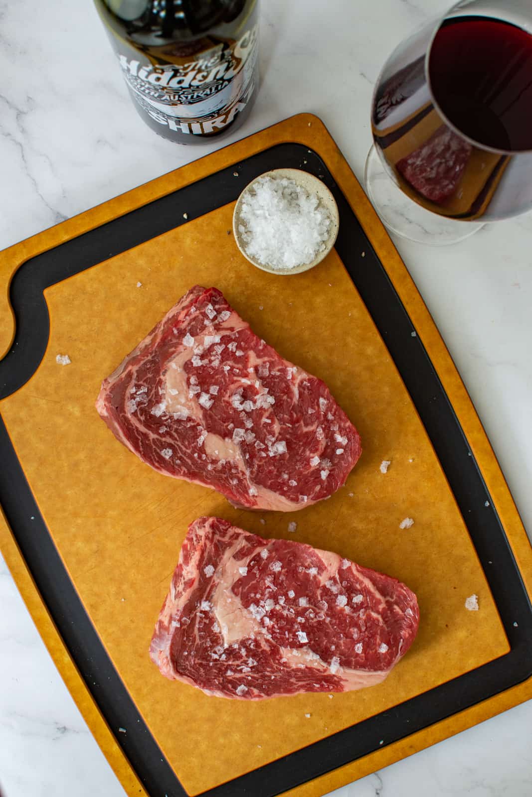 scotch fillet steaks on chopping board with hidden sea shiraz next to them 