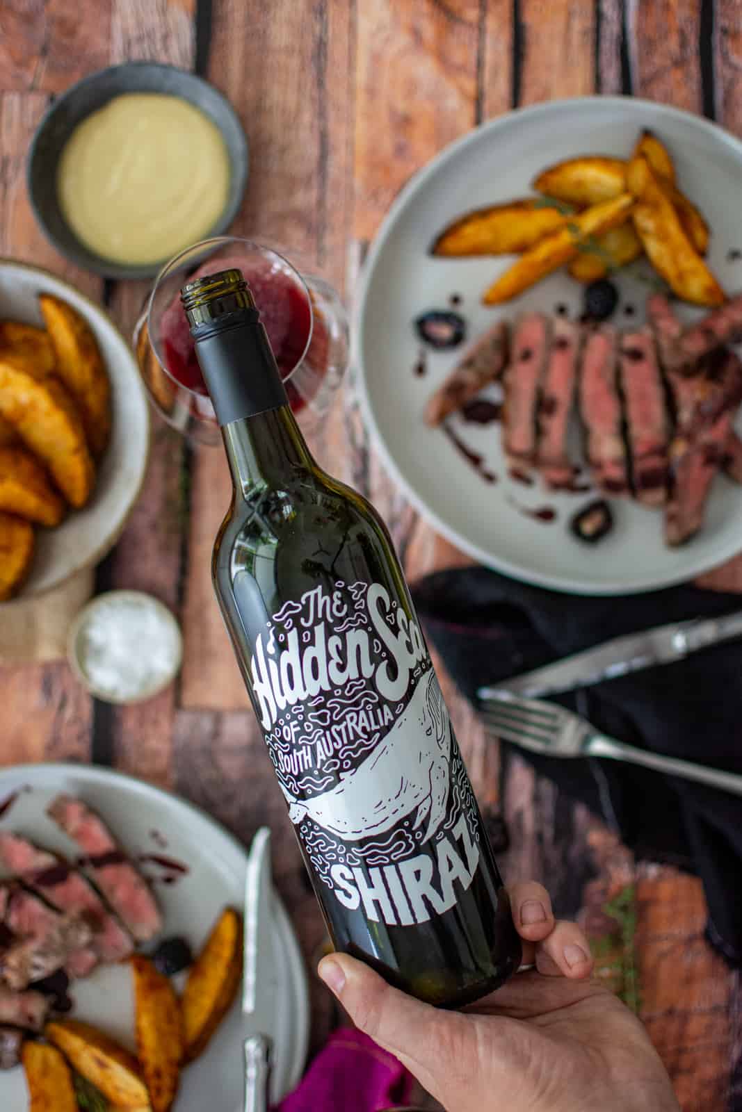 close up of the hidden sea shiraz with food below on a wooden table 