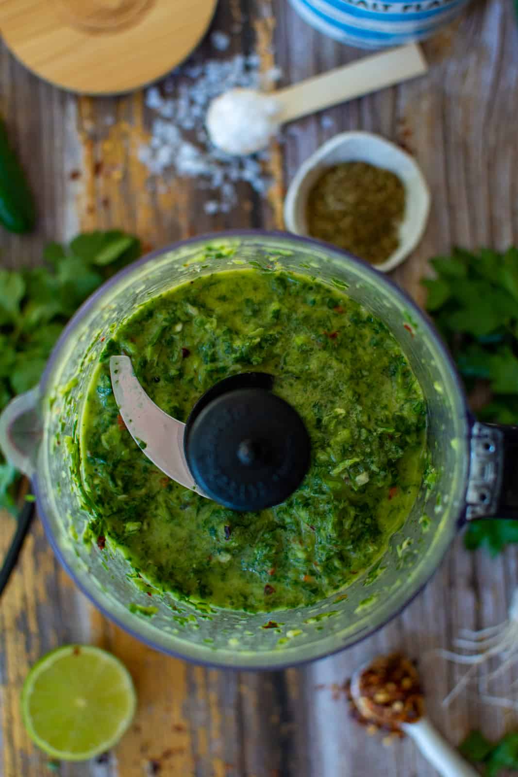 chimichurri in a food processor and the ingredients around it