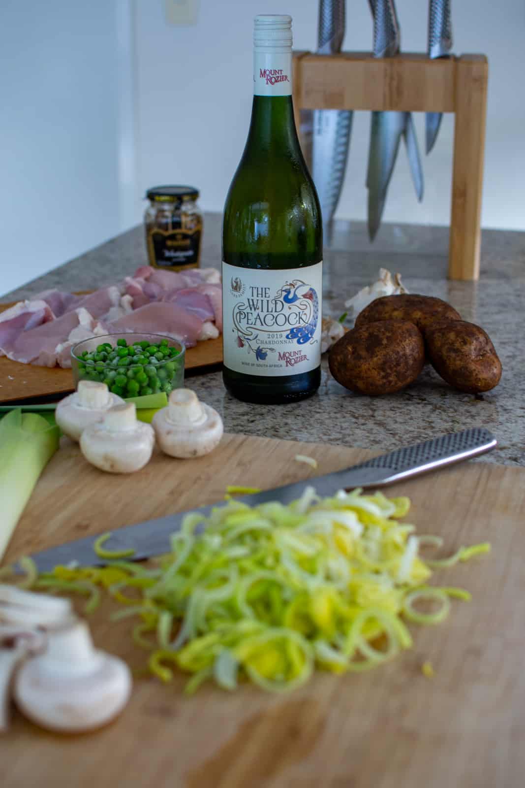 leeks chopped in a chopping board with other vegetables and a btl of wine in the background
