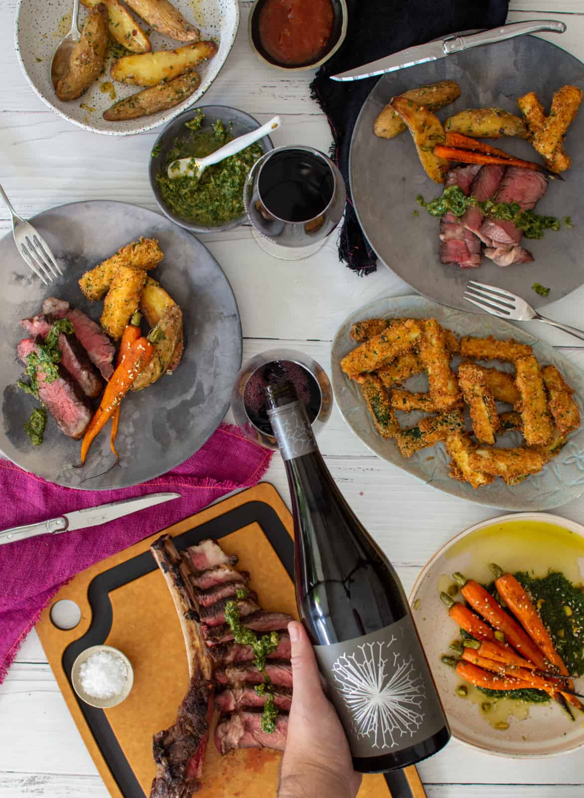 grilled tomahawk steak and sides on a table, wine being poured into a glass