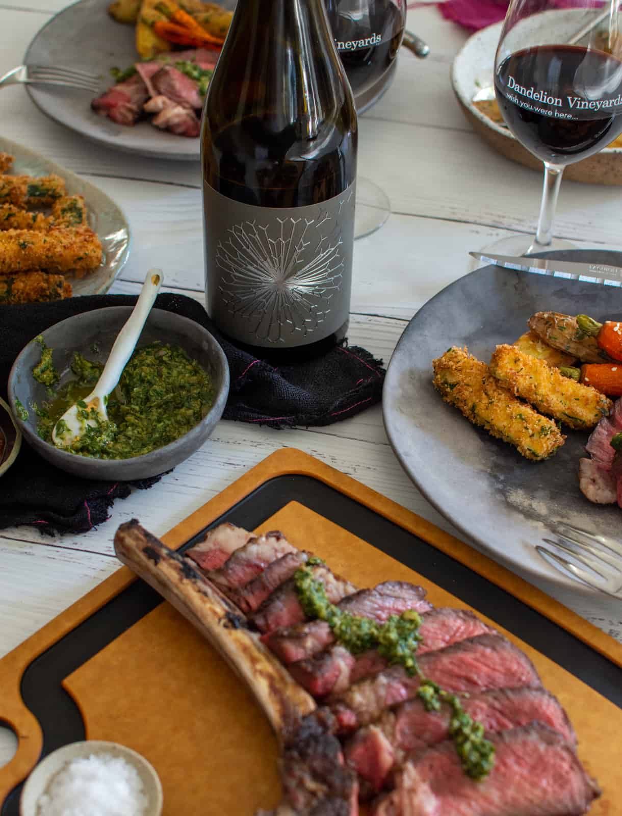 grilled tomahawk steak, wine and sides on a table