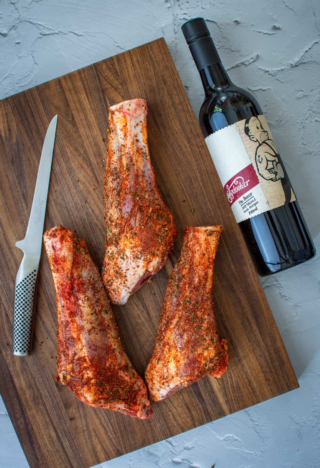 lamb shanks covered in a spice rub on a chopping board