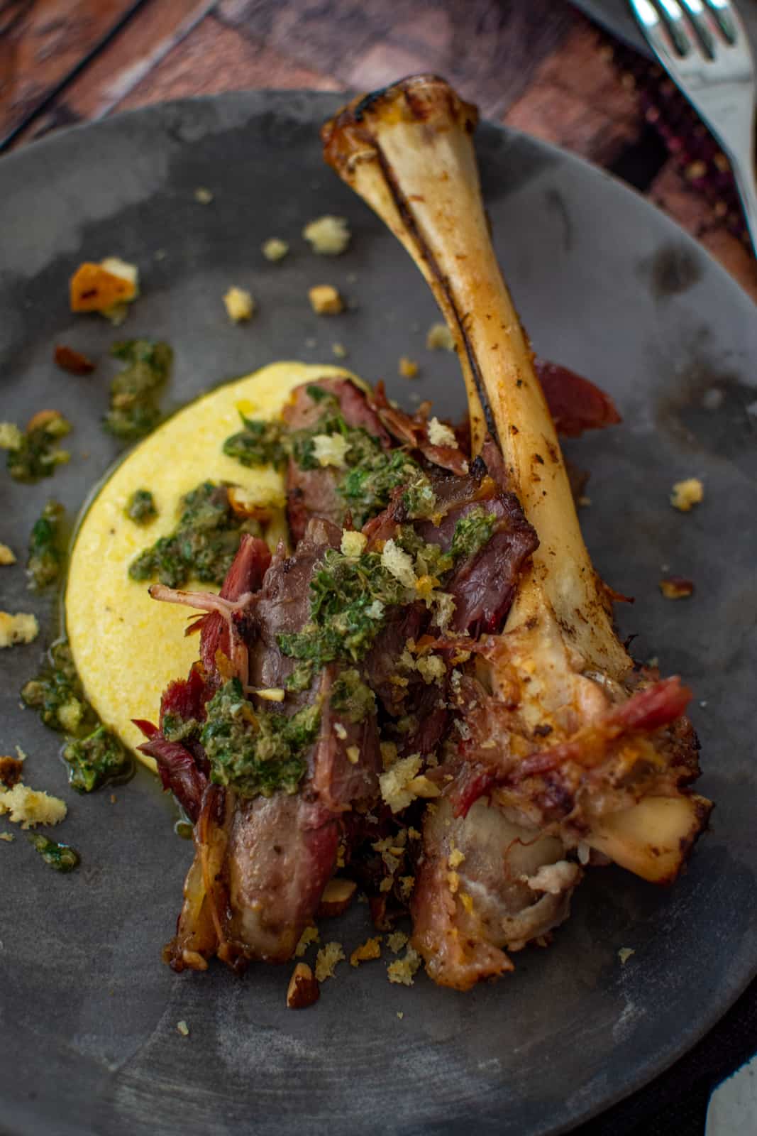 smoked lamb shank on a plate with polenta and anchovy dressing