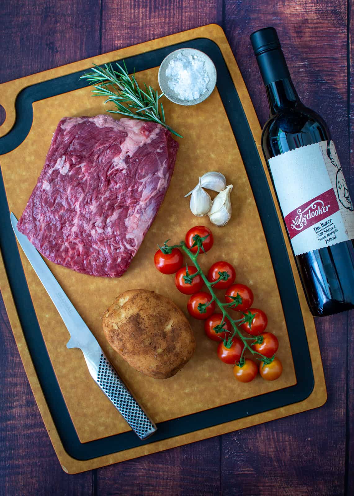 bavette steak, tomatoes & potato on chopping board. Red wine next to it