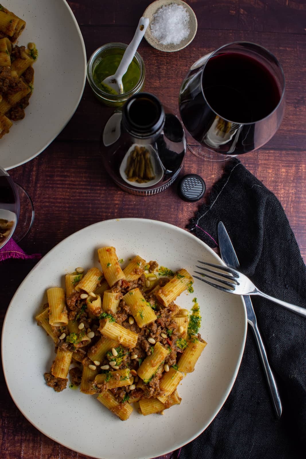 lamb ragu in a white bowl with wine, cutlery and black napkin next to it