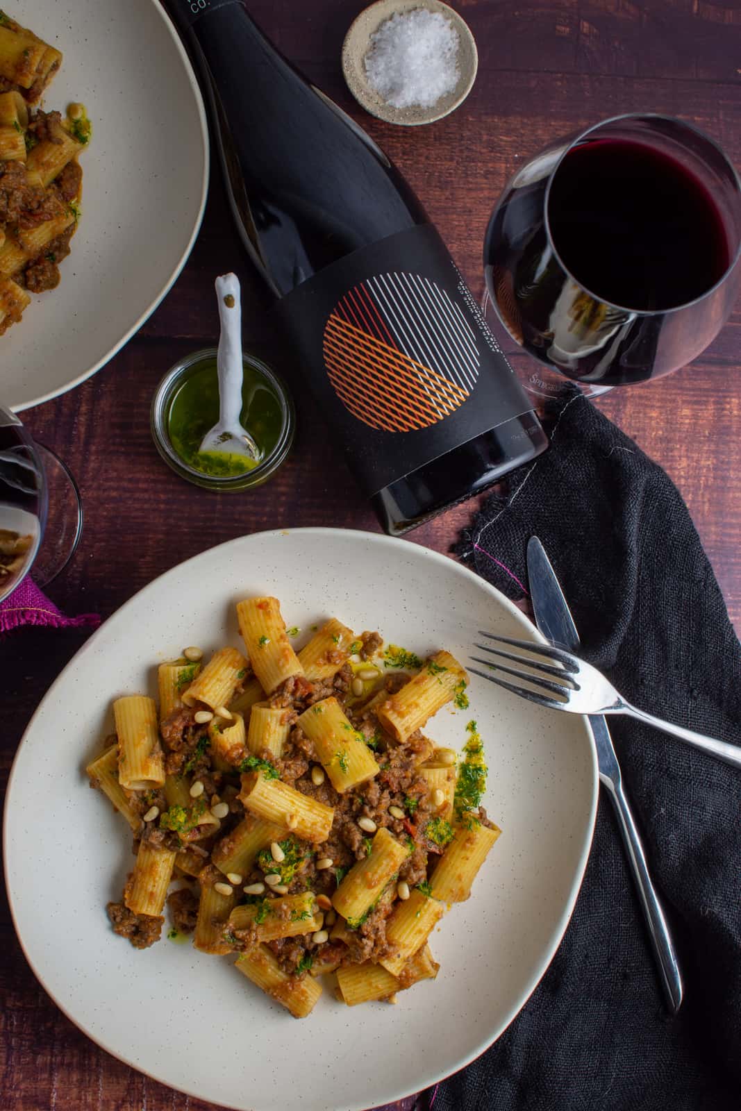 bowl of la,b ragu pasta on a table with black napkin and red wine next to it 