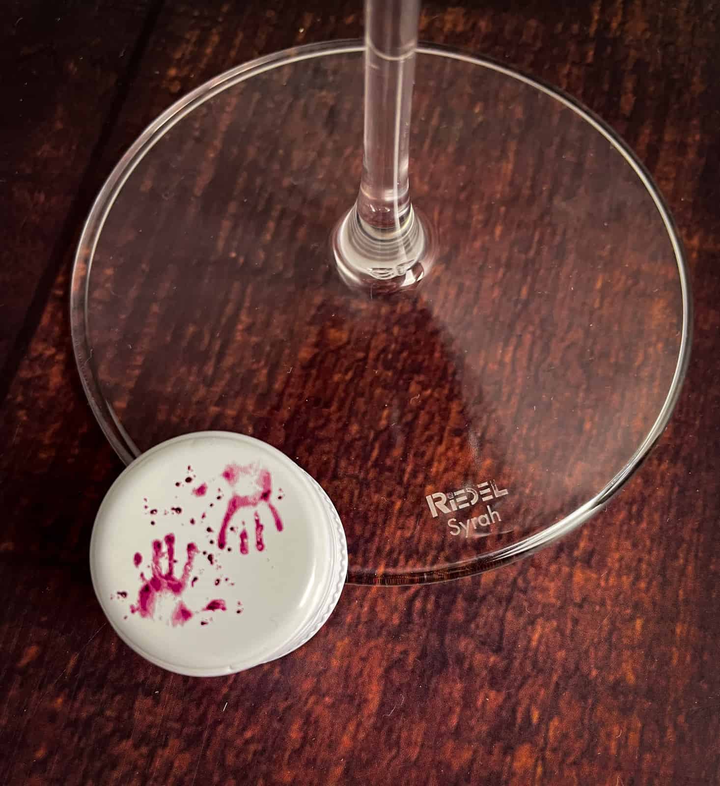close up of purple hands bottle cap and riedel wine glass