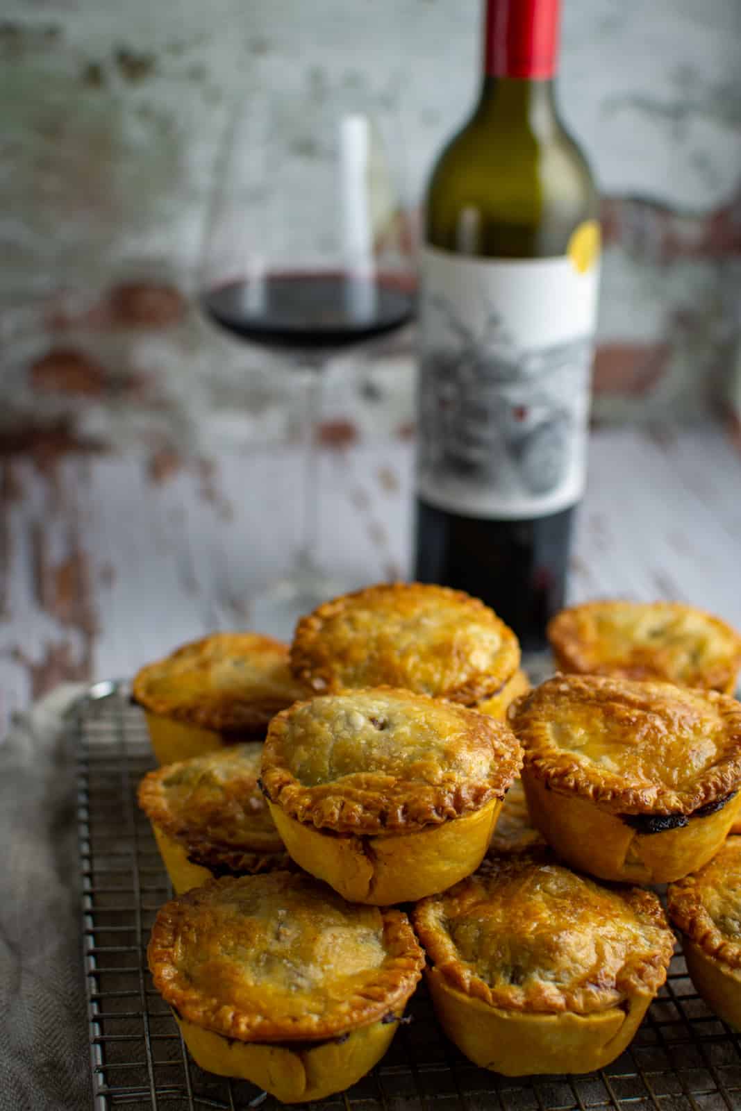 beef pies on top of each other on wire rack - wine in background