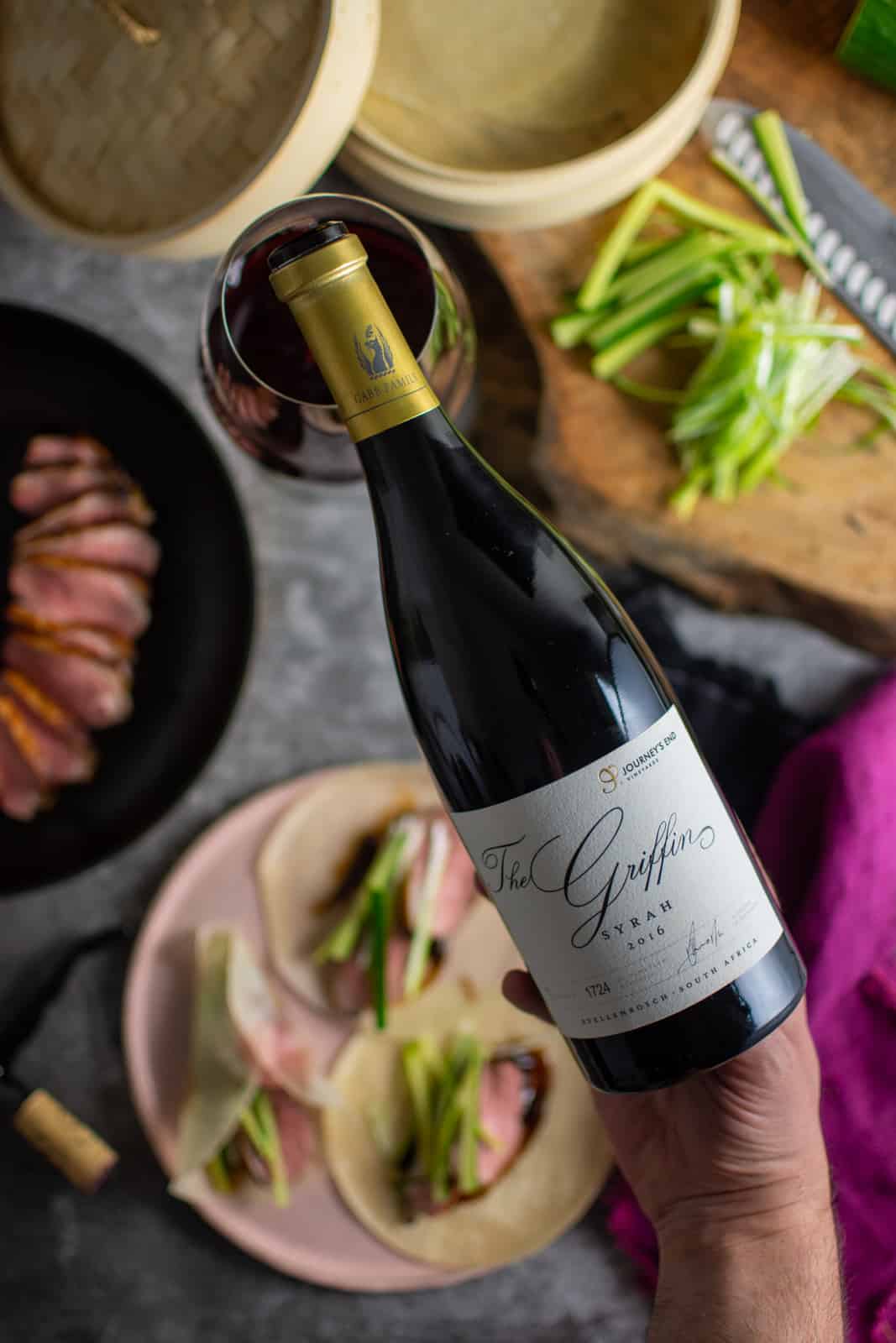 someone pouring journeys end griffin syrah with blurred food below