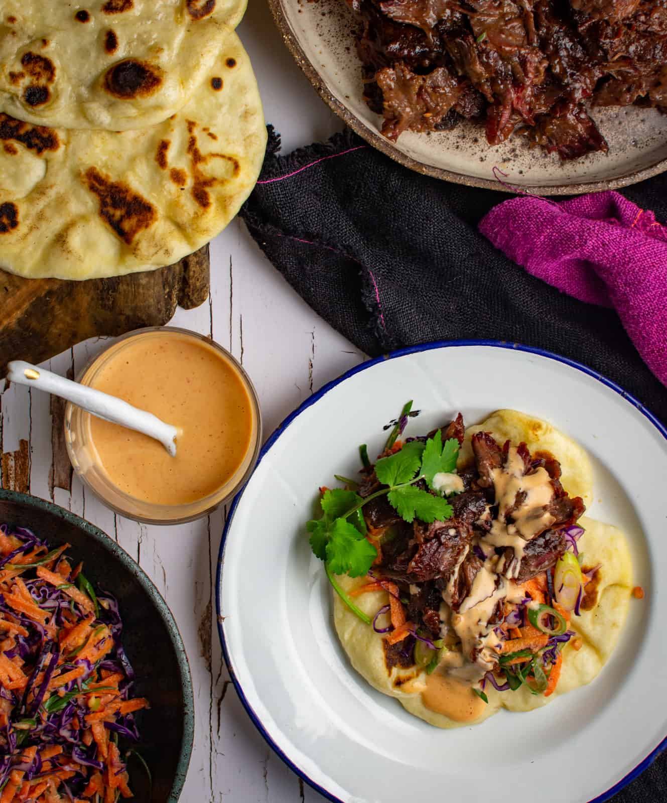 smoked beef cheeks pita on a plate next to more pitas, slaw and sauce