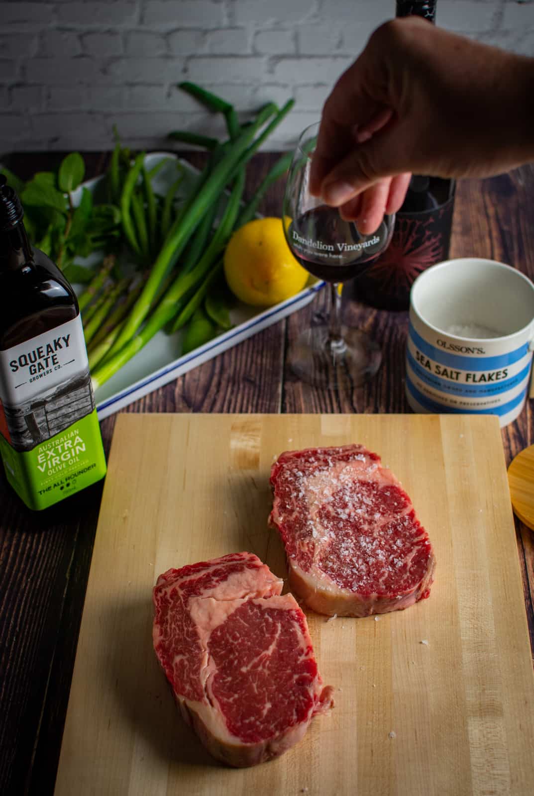 salted steak on a chopping board, red wine and mixed greens beside it