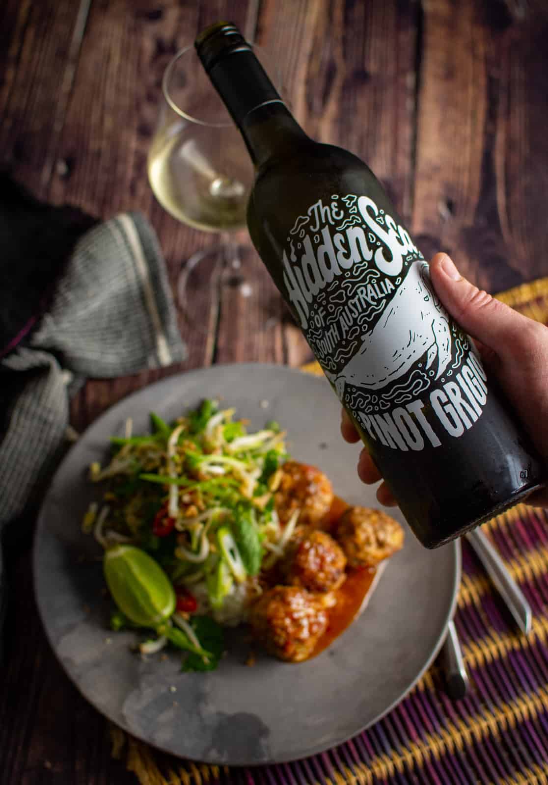 someone pouring hidden sea pinot grigio with food blurred below 