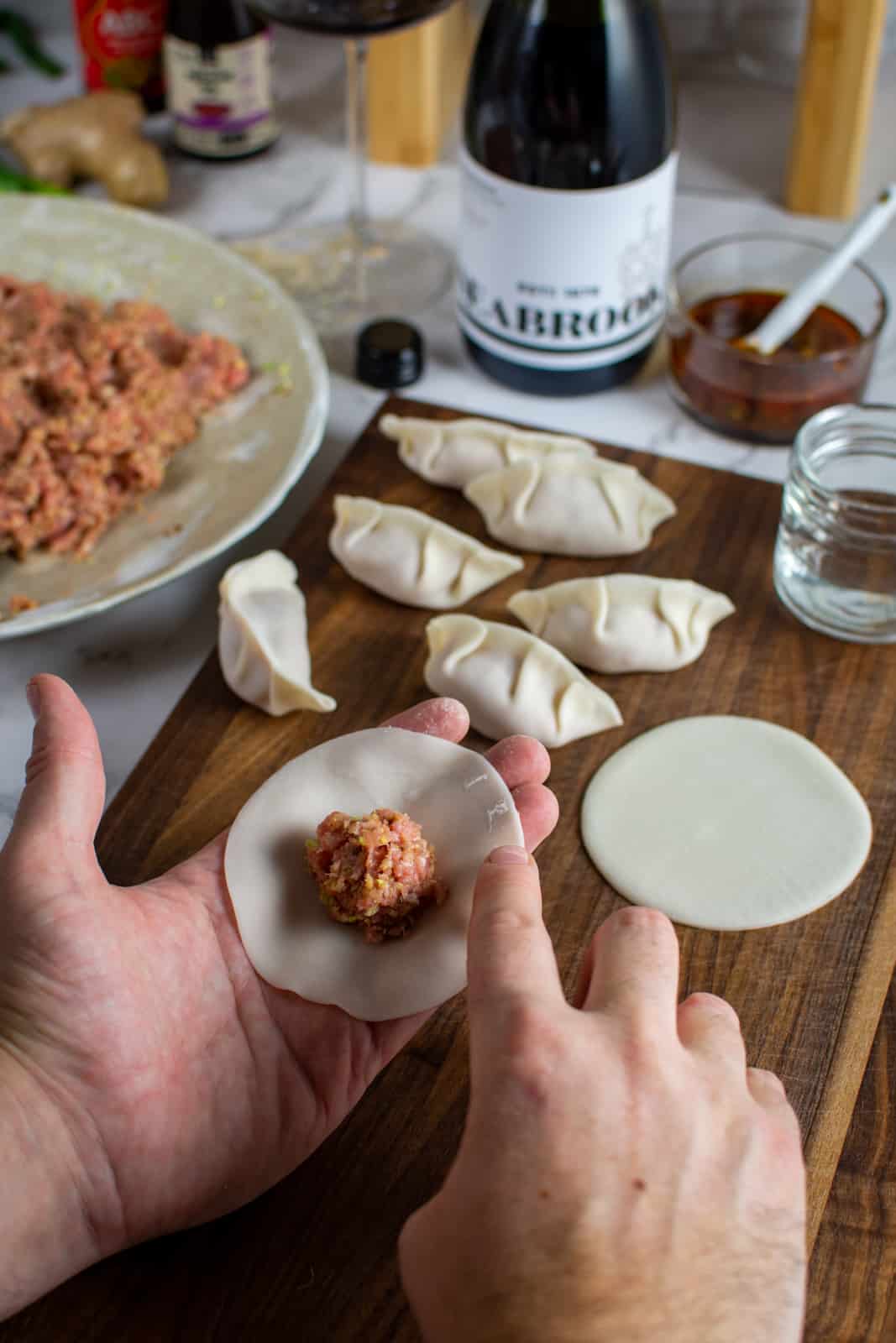 someone holding a dumpling wrapper and wiping water around the edges