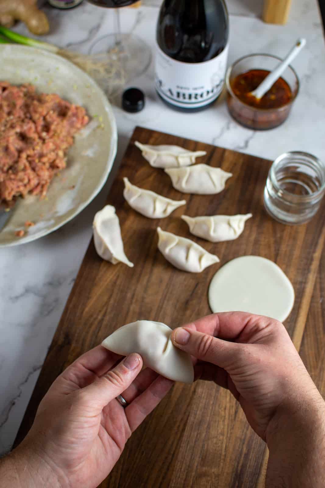 Someone pleating a dumplng wrapper with made dumplings and pork cabbage dumpling mixture in the background