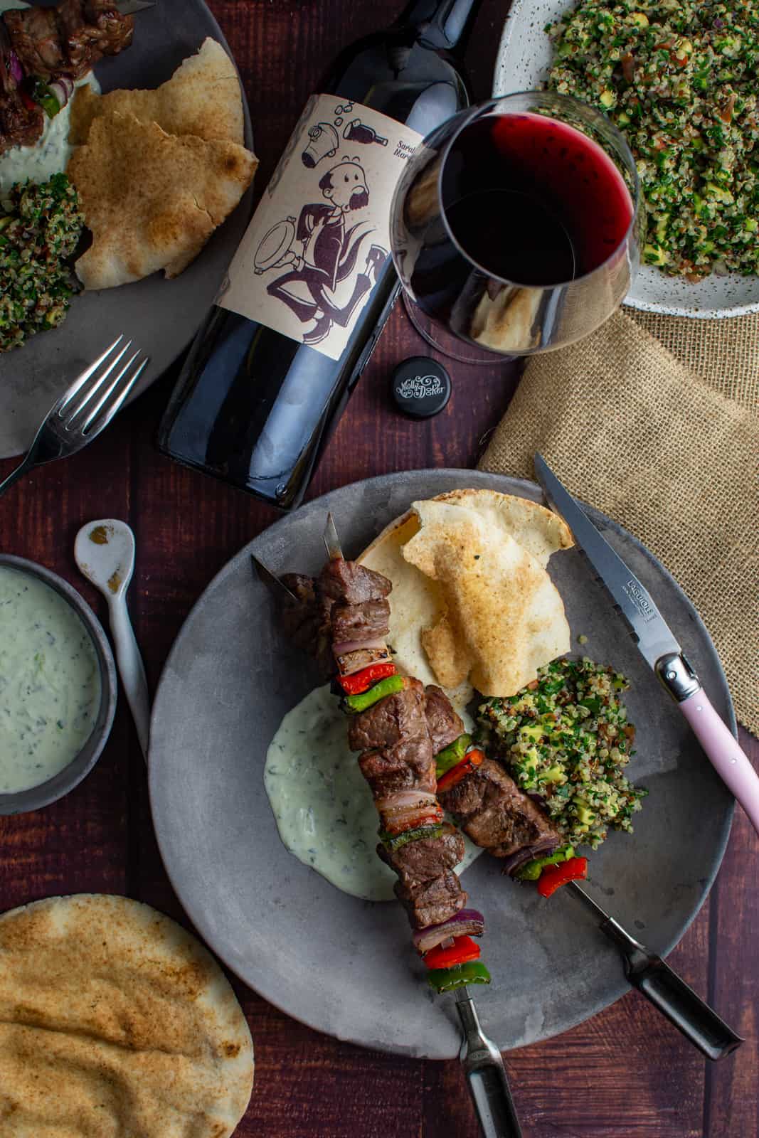 birdseye view of lamb kebabs on a plate with tabbouleh, yoghurt dressing and pita