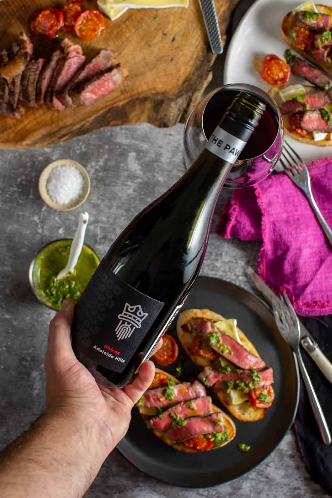 someone pouring a glass of wine with steak crostini in background