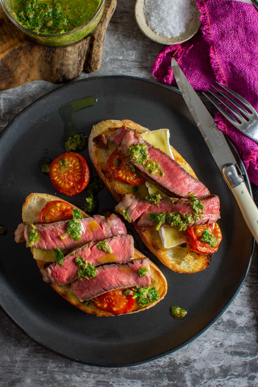 birdseye view of syeak crostini on a black plate with cutlery and coloured napkins