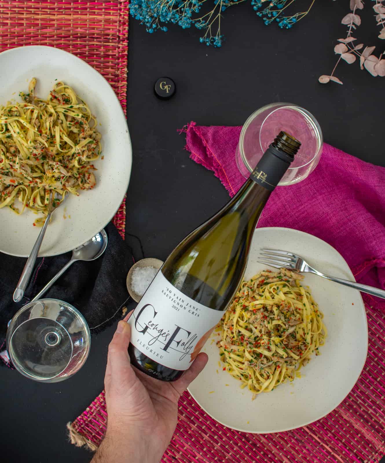 Someone pouring  glass of wine with bowls of pasta below