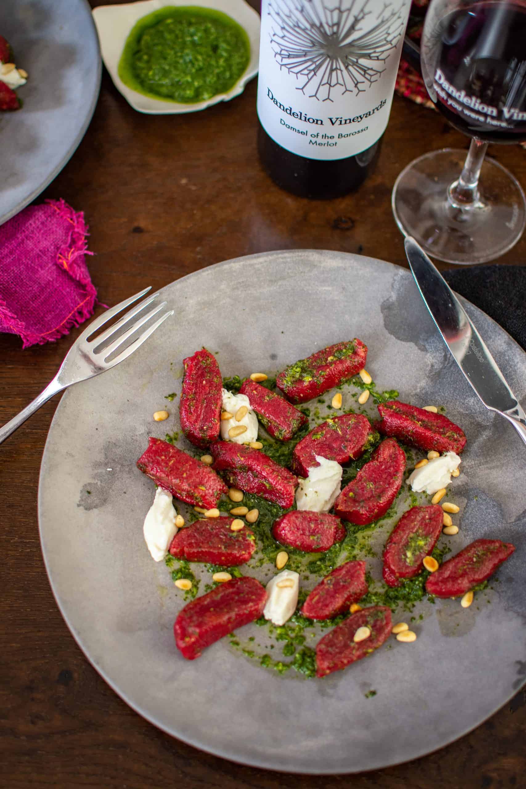 A plate og beet gnocchi, wine glass and dandelion vineyard red wine on wooden table