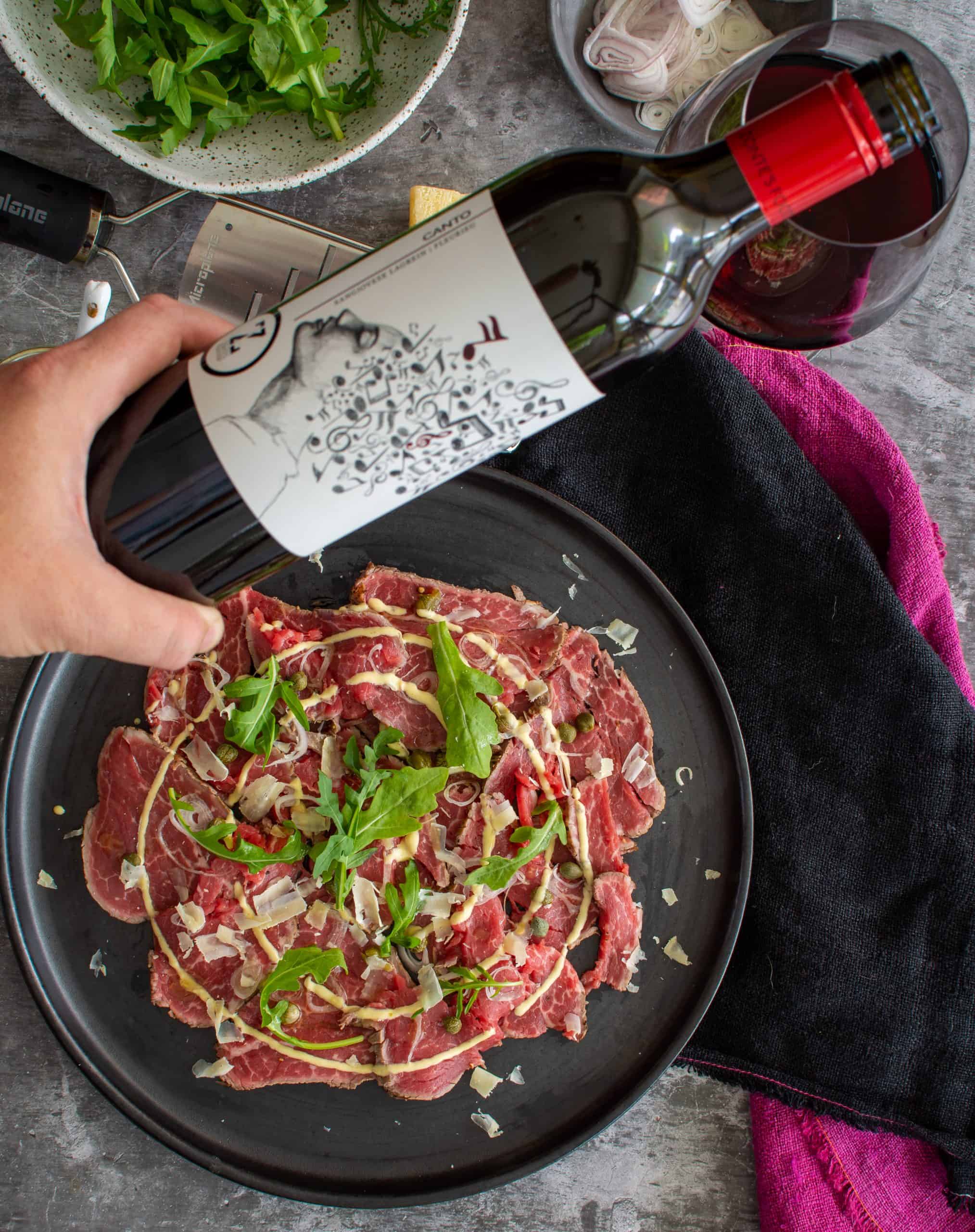 someone pouring red wine with food below on a table