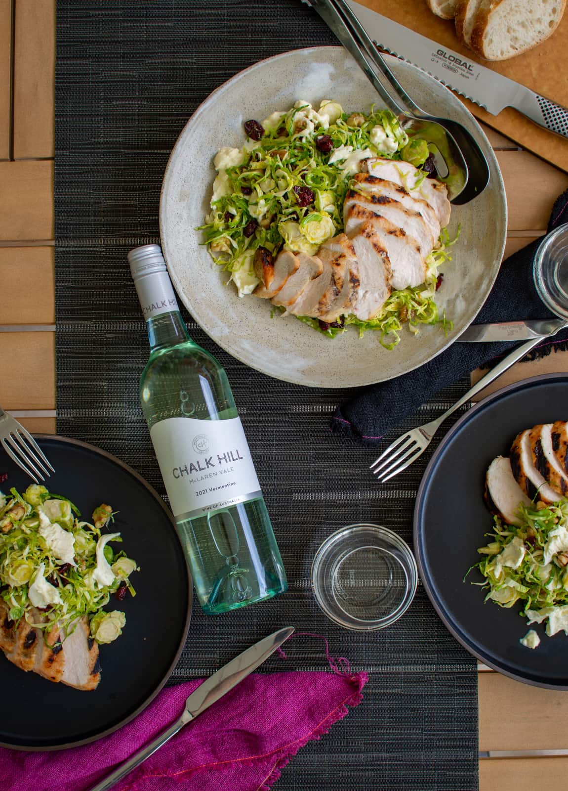 birds eye view of bowls & plates with shaved brussels sprout salad on a table with chalk hill vermentino bottle lying down too