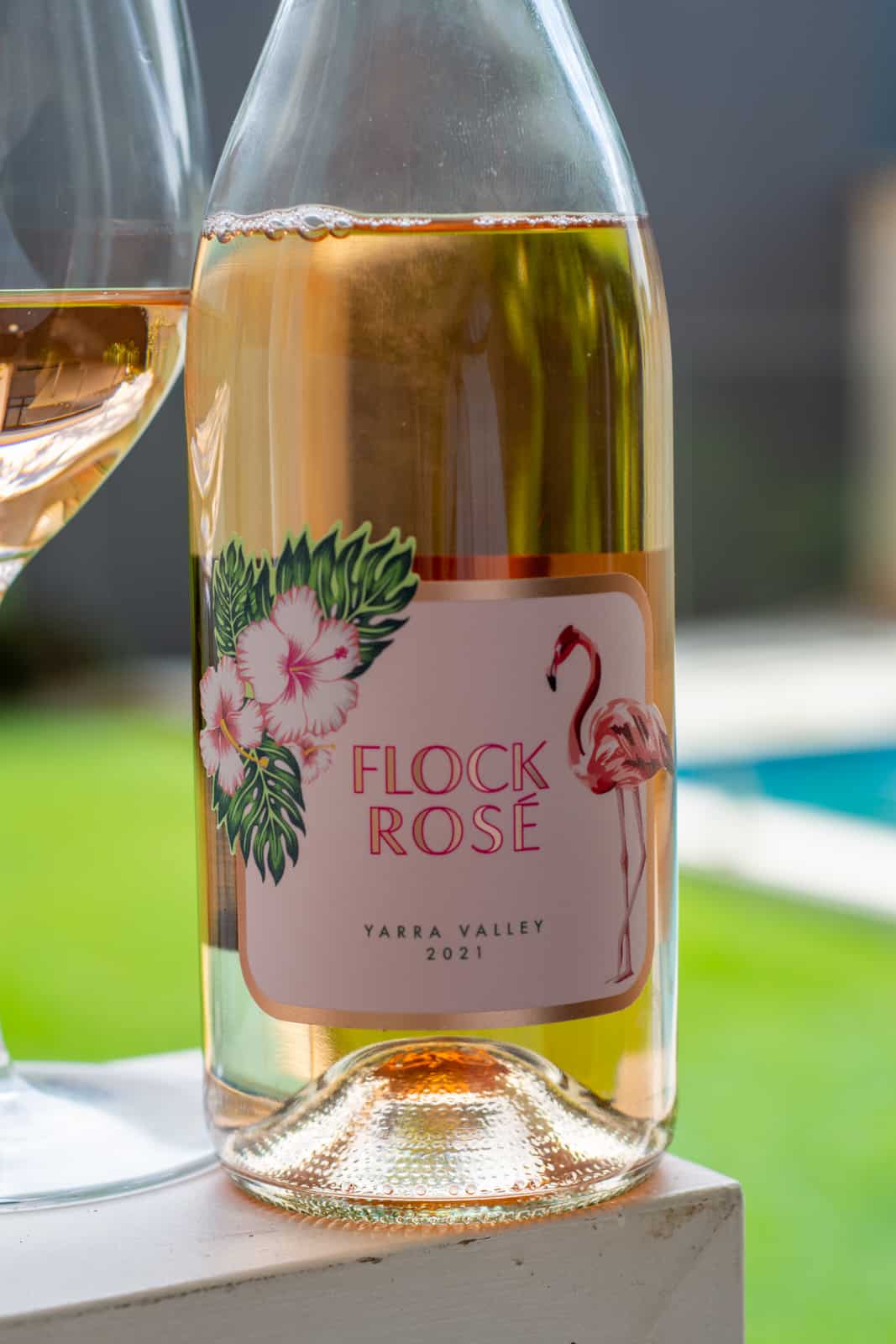 A bottle of flock rose with wine glass beside and swimming pool blurred in background