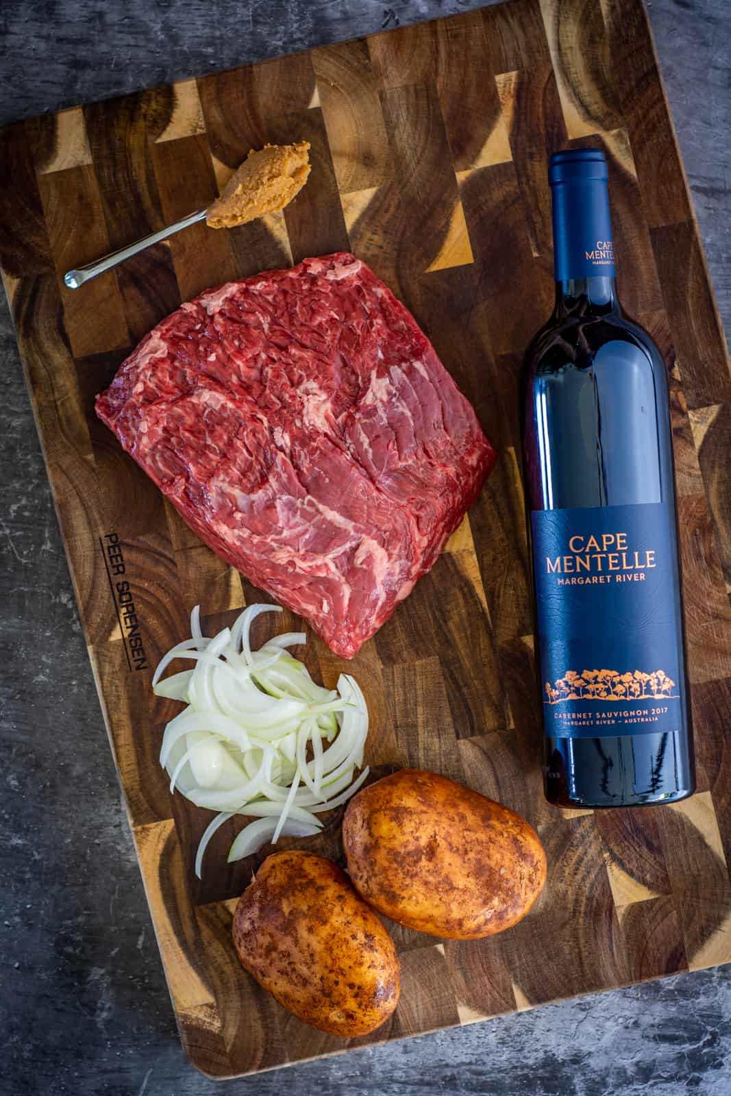 birdseye view of bavette steak, onions, miso, potatoes and red wine on a chopping board