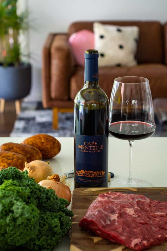 bavette steak on a chopping board with vegetables next to it and a bottle of wine