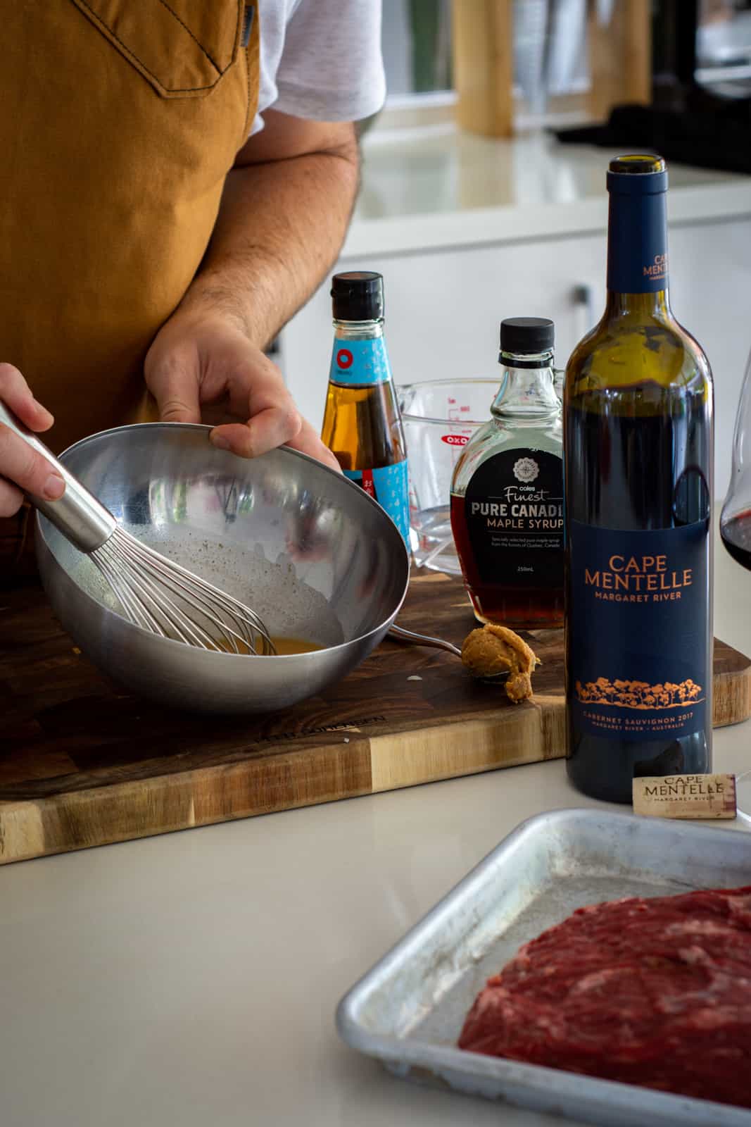 someone whisking miso dressing in the kitchen with ingredients and red wine on counter top