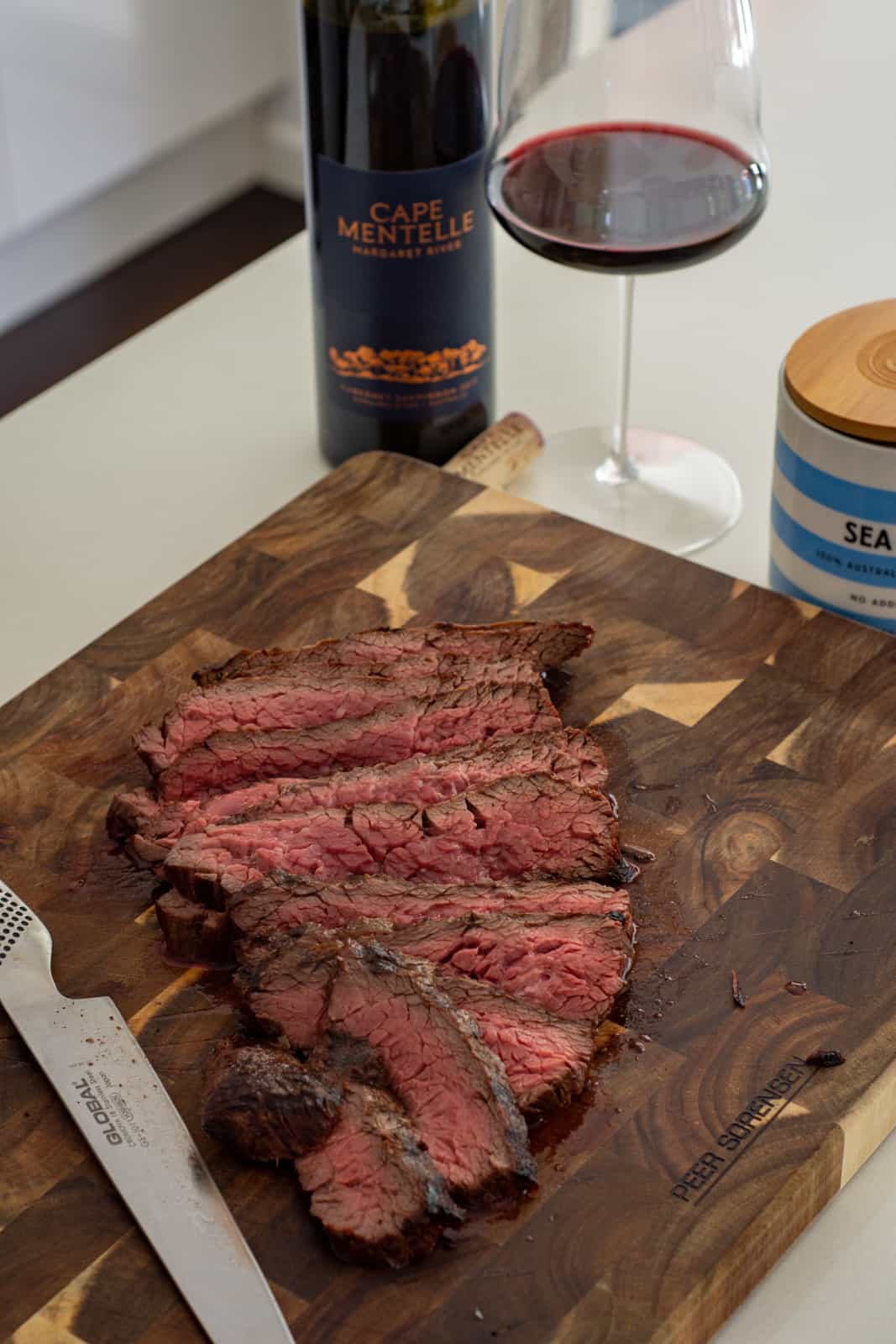 sliced bavette steak in a chopping board with a bottle of wine beside it