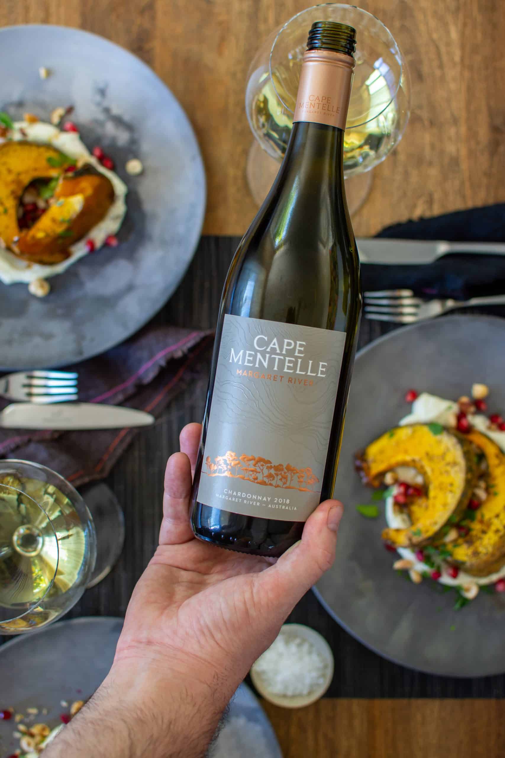 someone pouring a cape mentelle chardonnay with plates of food below