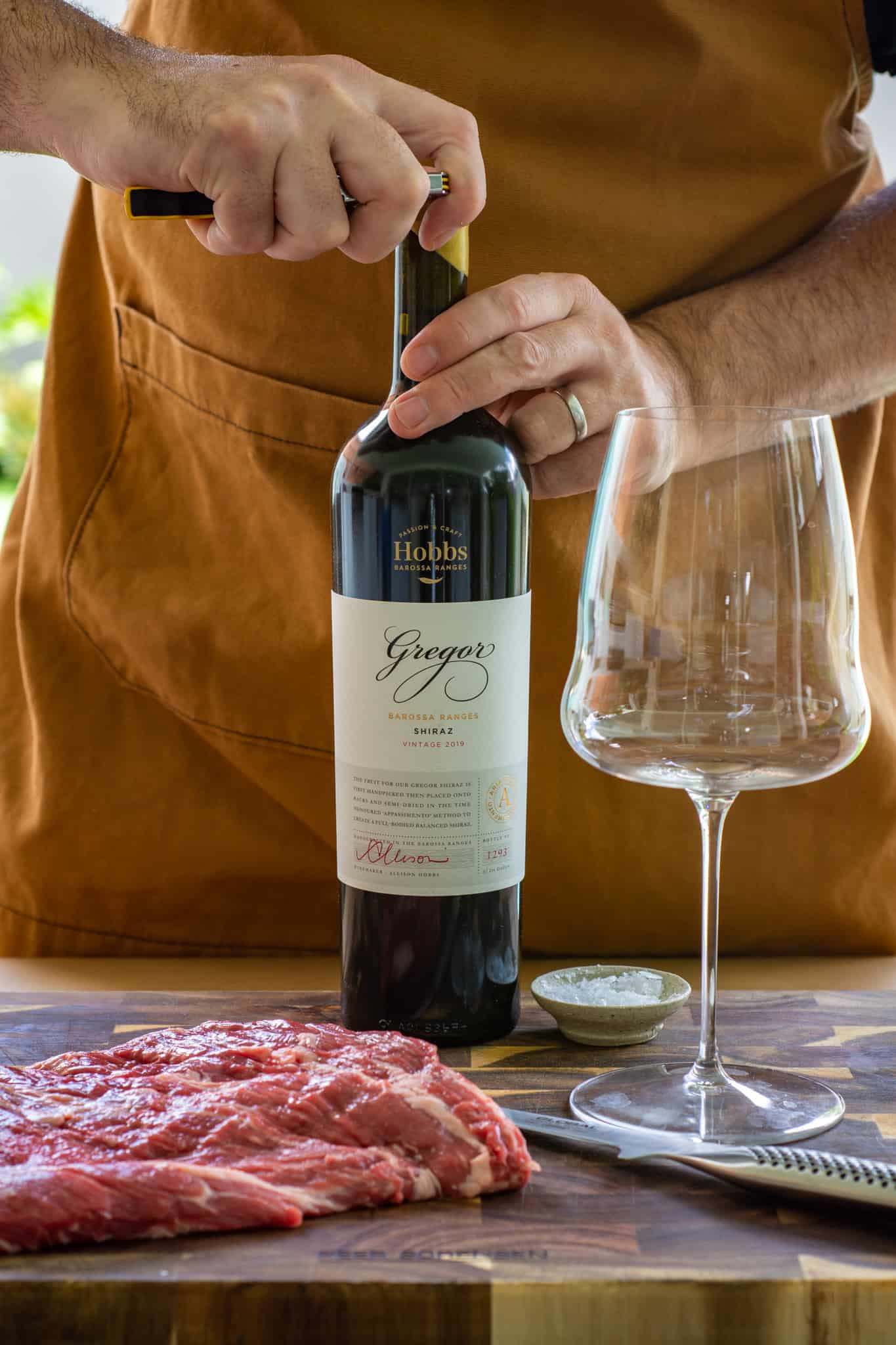 someone opening a bottle of wine with flap steak on a chopping board