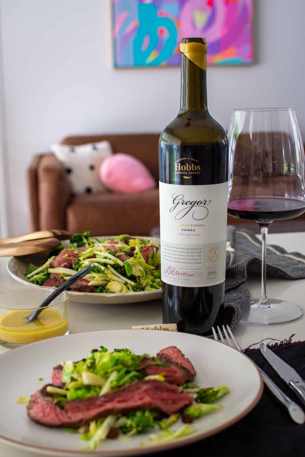 broccoli, steak & pear salad on white plates on counter top, red wine and glass on counter top too