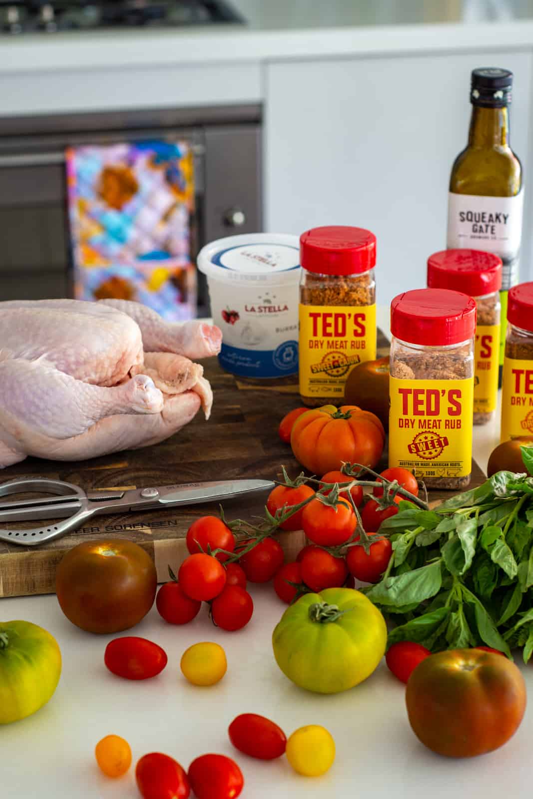 whole chicken on a board surronded by tomatoes, teds bbq rubs and basil