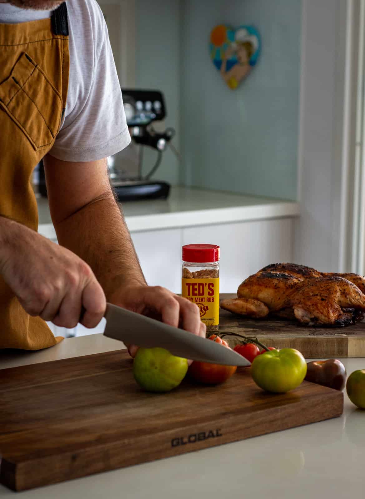 Someone chopping tomatoes with a cooked chicken in background