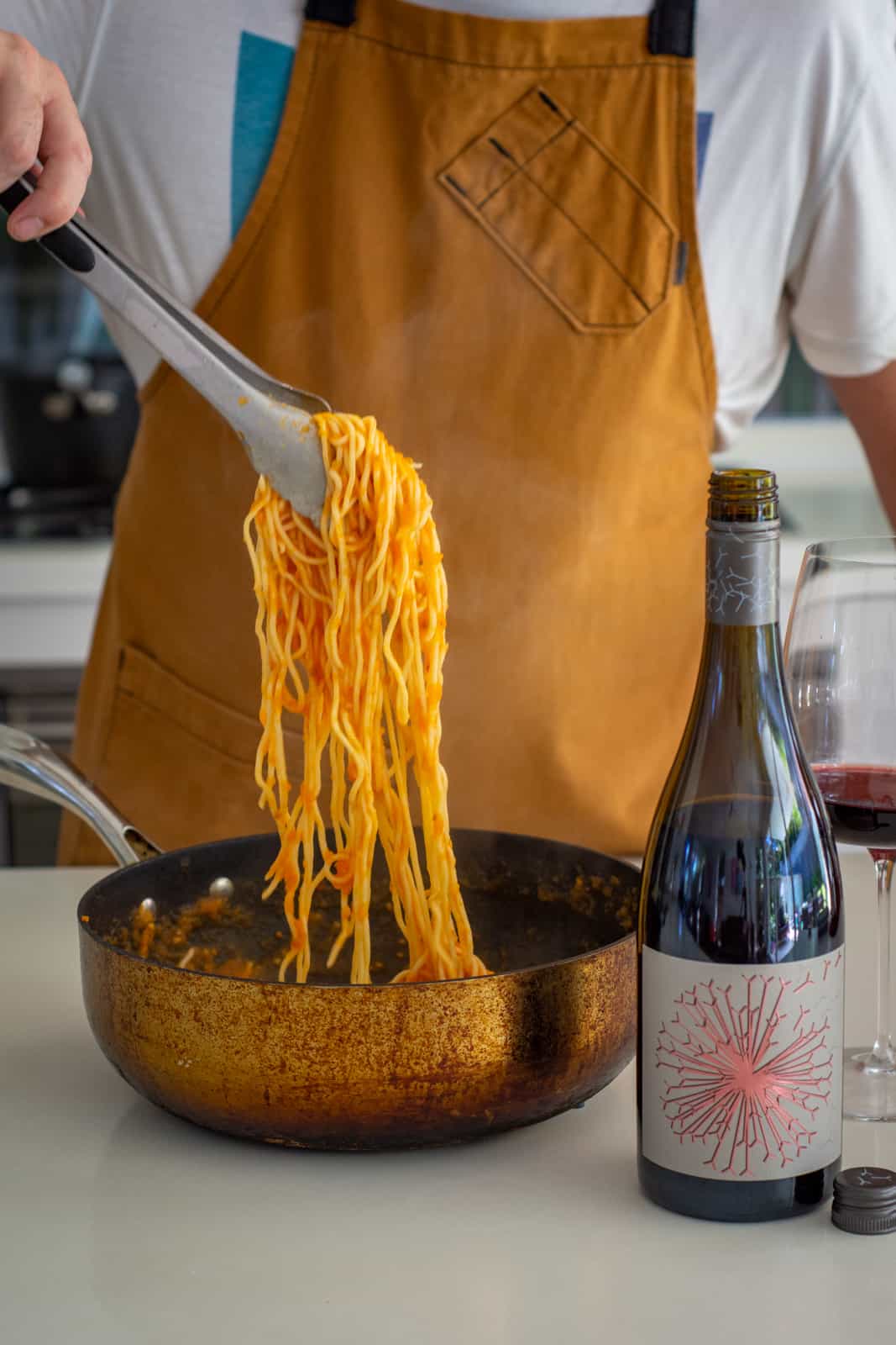 Someone holding spaghetti over a bowl in the kitchen