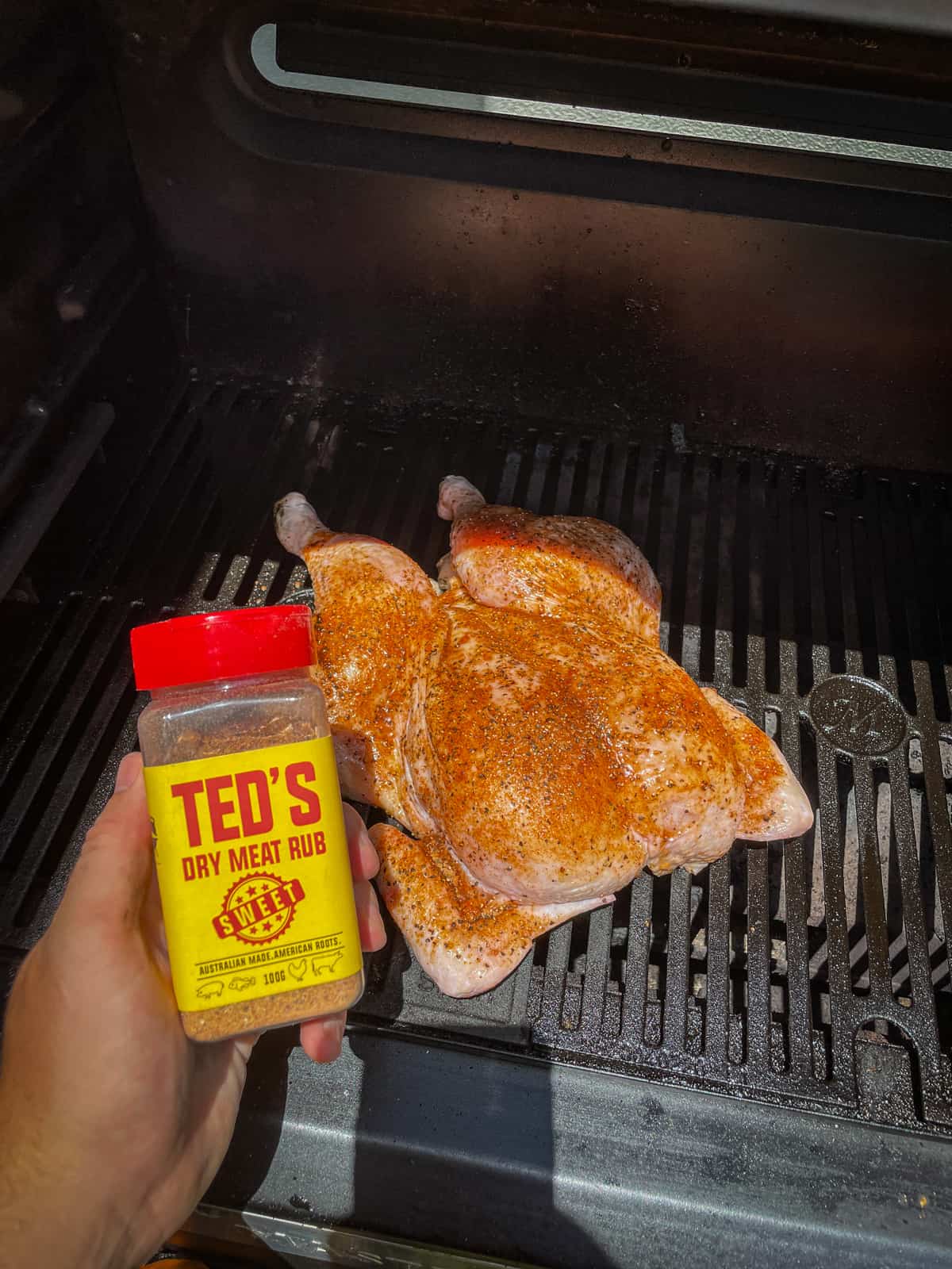 Someone holding teds dry rub with a BBQ chicken in background
