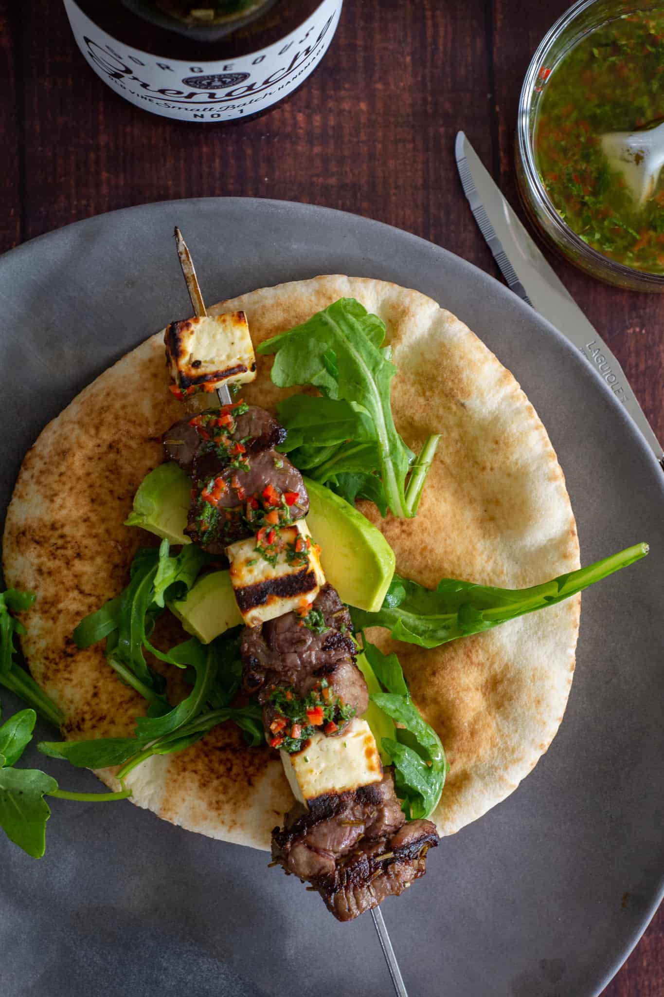 Grilled lamb skewer with halloumi on a pita bread with wine and salsa next to the plate