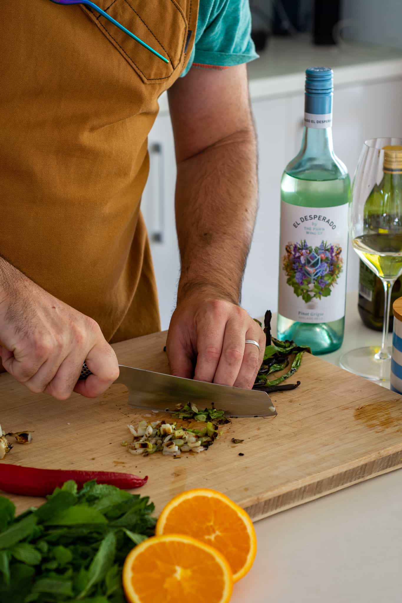 someone chopping spring onions in the kitchen with orange, chilli and mint beside them