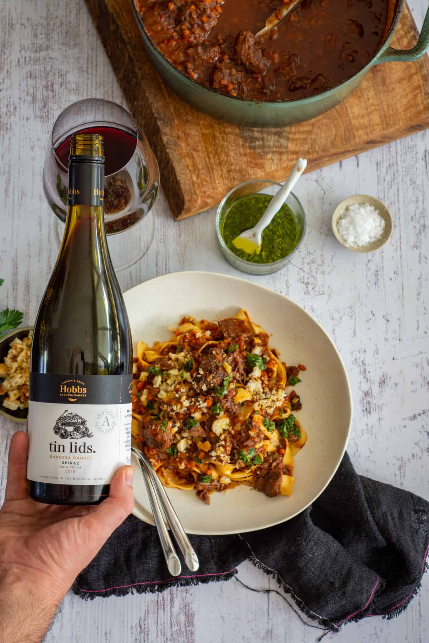 someone pouring a glass of Hobbs wine with food in a bowl below them 