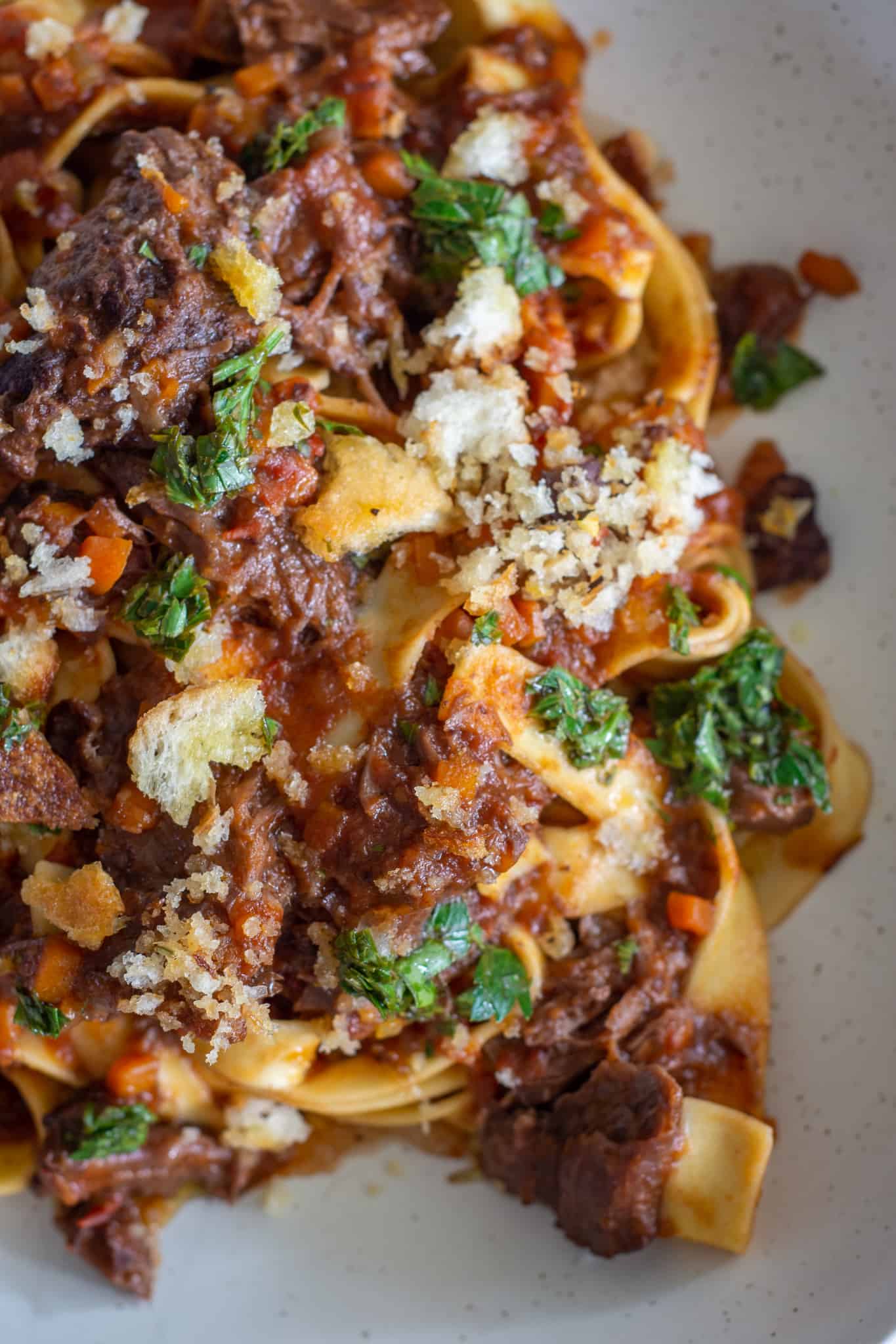 Close up of beef cheek ragu topped with lemon parsley oil and breadcrumbs 