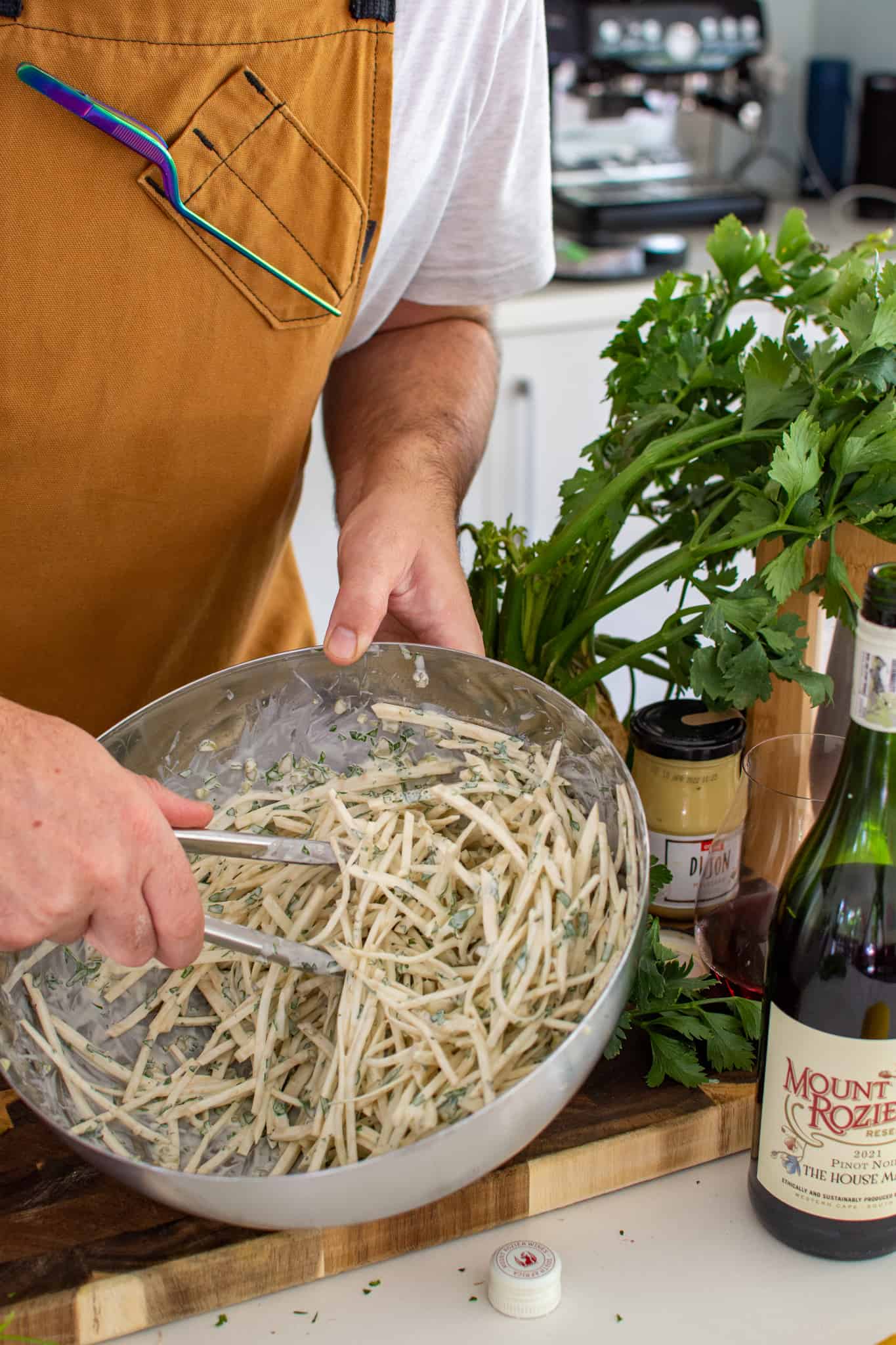 Someone tosshing celeriac remoulade in a bowl in the kitchen