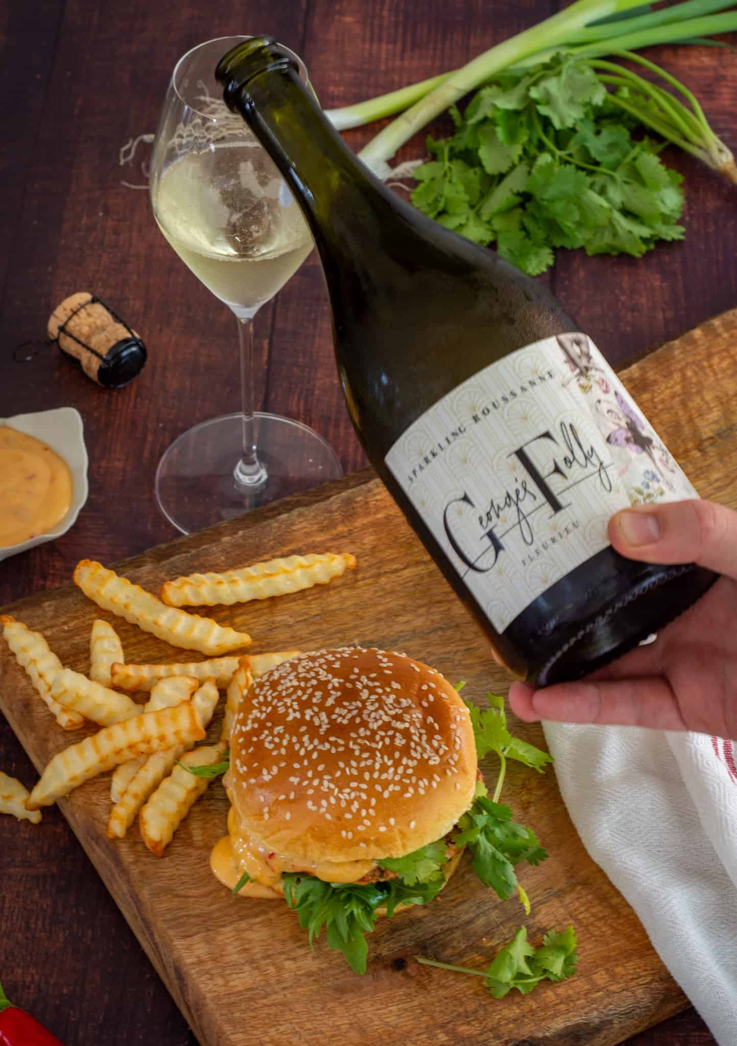 someone pouring sparkling wine with a burger and chips below