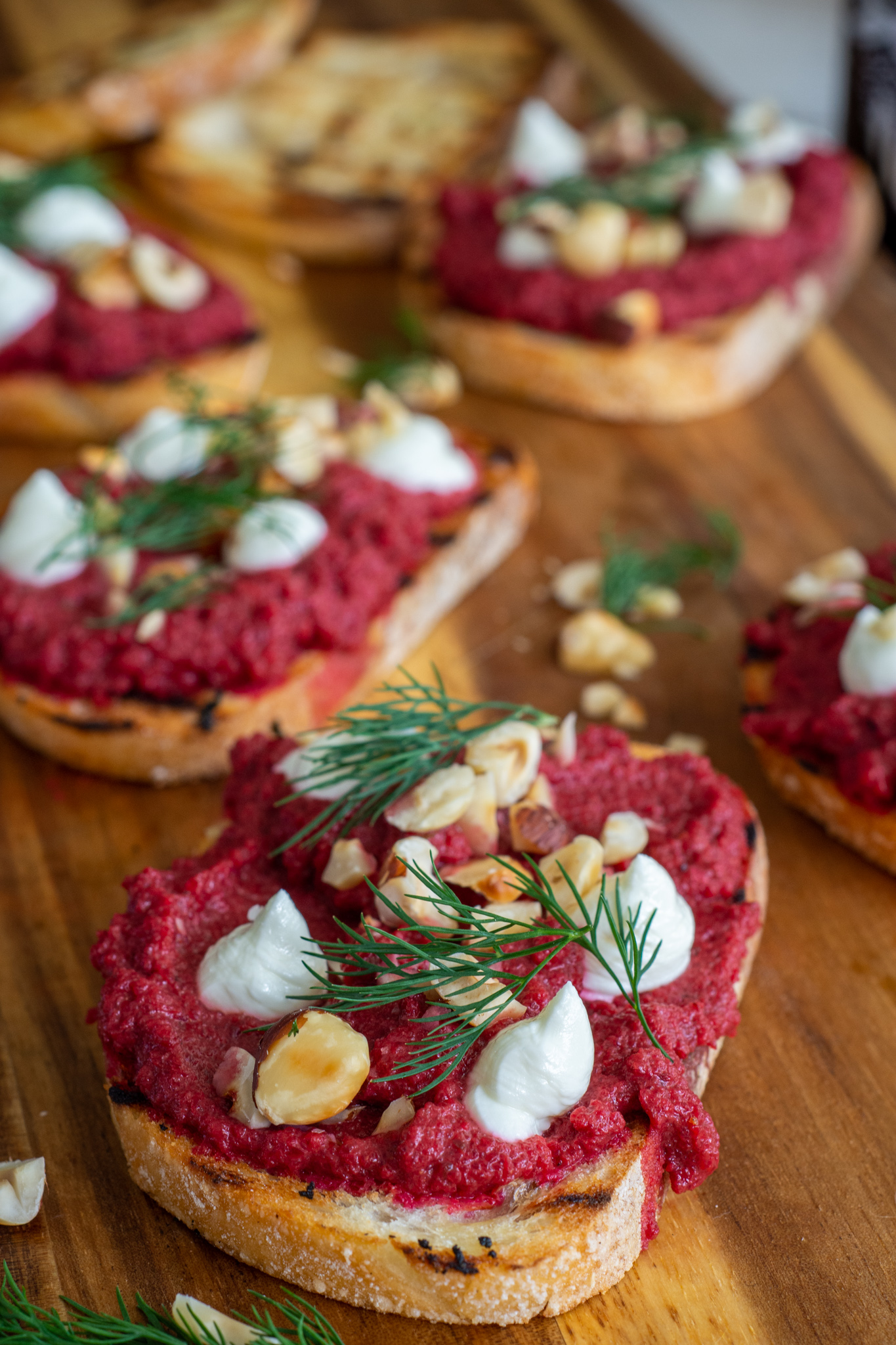fancy toast on a chopping board. beetroot, whipped goat cheese and hazelnuts on toast