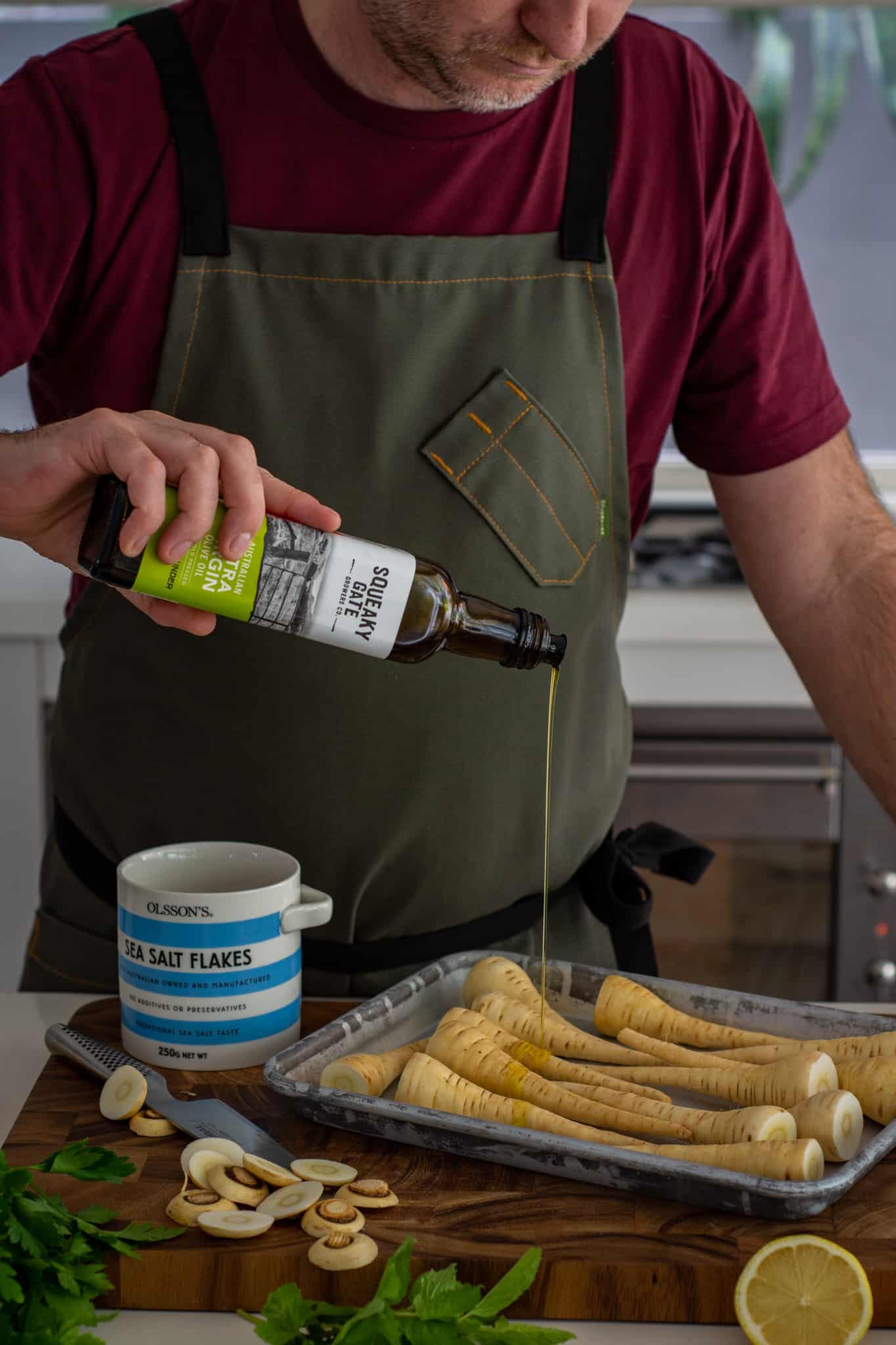 someone drizzling olive oil over a tray of parsnips in the kitchen