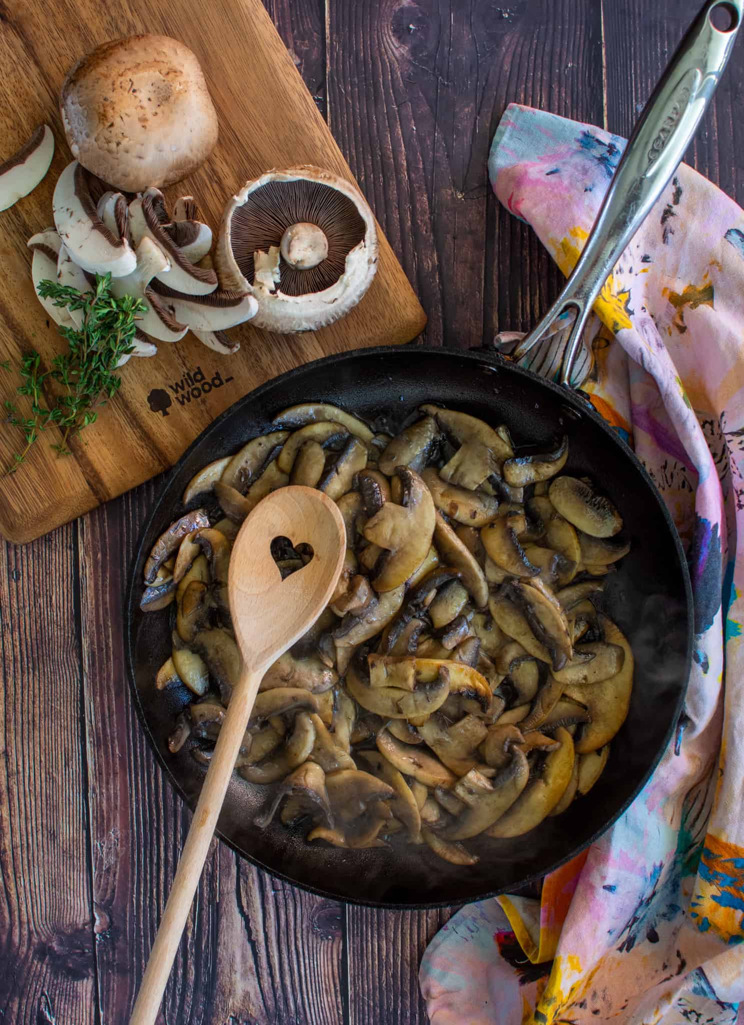 mushrooms in a frying pan with chopping board beside with mushrooms on it