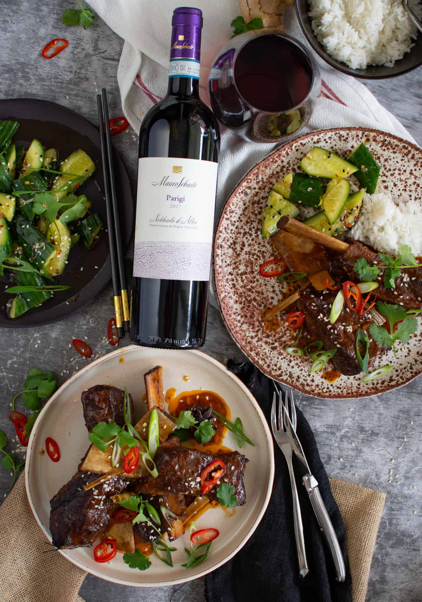 Birdseye view of Asian braised beef short ribs on a plate with cucumber salad and rice in bowls beside