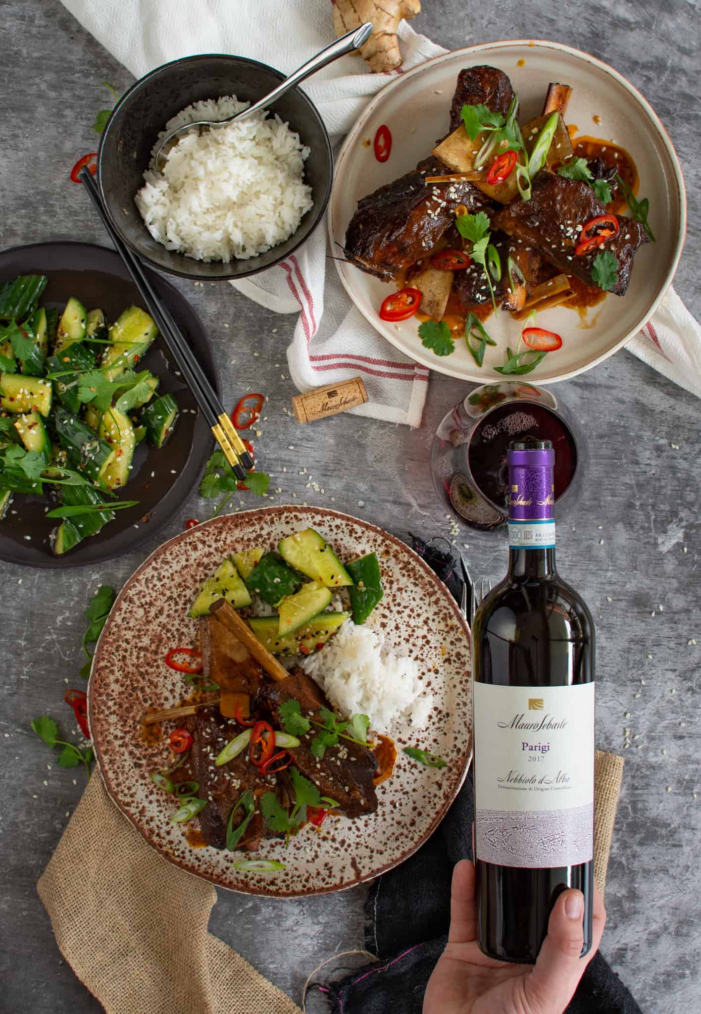 someone pouring wine into a glass with Asian slow cooked beef ribs on a plate next to the wine